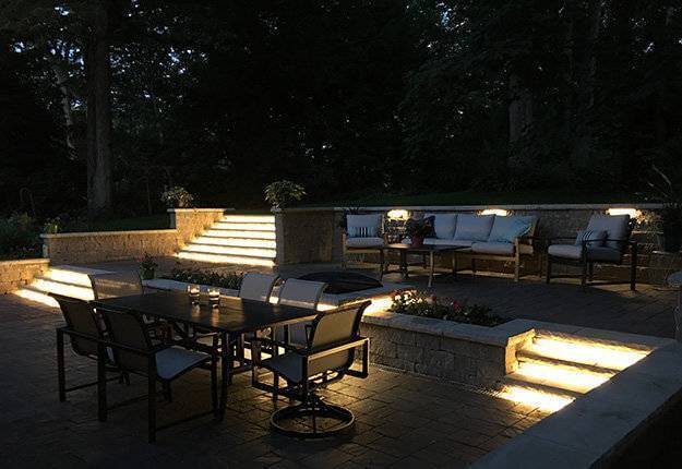 beautiful multilevel outdoor patio at nighttime with patio furniture and custom lighting on the patio steps
